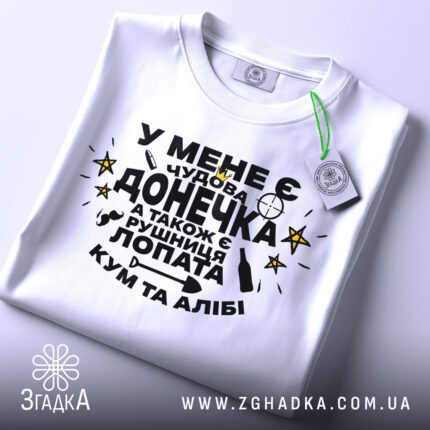 Футболка чудова донечка, біла, зображена зверху, фон світло-сірий, принт чорного кольору з жовтими зірками, текст українською мовою, на комірці є етикетка.