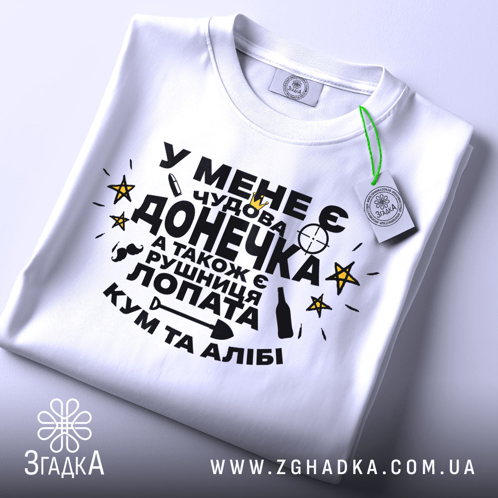 Футболка чудова донечка, біла, зображена зверху, фон світло-сірий, принт чорного кольору з жовтими зірками, текст українською мовою, на комірці є етикетка.