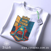 Футболка дайте спокій, біла, лежить на столі, фон світлий, принт з лягушкою на кріслі, з текстом 'Дайте мені спокій', з етикеткою на шнурку.