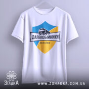 Футболка далекобійники України, білого кольору, підвішена на вішалці, фон світло-сірий, принт з синім та жовтим щитом, малюнком вантажівки та написом 'ДАЛЕКОБІЙНИКИ УКРАЇНИ'.