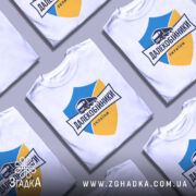 Футболка далекобійники України, білого кольору, зображена на манекені з правого боку, фон світло-сірий, принт містить синій та жовтий щит з малюнком вантажівки та написом 'ДАЛЕКОБІЙНИКИ УКРАЇНИ'.