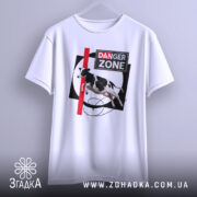 Футболка Danger Zone білого кольору, підвішена на вішалці, ракурс спереду, фон світлий, принт з коровою, червоною лінією та написом 'DANGER ZONE'.