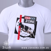 Футболка Danger Zone білого кольору, складена на поверхні, ракурс зверху, фон світлий, принт з коровою, червоною лінією та написом 'DANGER ZONE', з етикеткою на комірці.