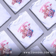 Футболка давай гратись, білого кольору, зображена з фронтального ракурсу на манекені, фон світло-сірий, принт з чотирма мультяшними тваринами та касетою, текст 'давай гратись' виконаний рожевим кольором.