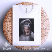 Футболка Давид арт, біла, складена на плетеній кошику, фон світло-сірий, принт зображає статую Давида з язиком, що висунений, та рукою, що торкається обличчя.