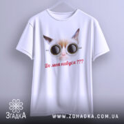 Футболка де моя кавуся. Біла футболка з принтом кота в окулярах, підвішена на вішалці. Фон світло-сірий, принт яскравий, текст червоним шрифтом, футболка має вільний крій.