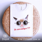 Футболка де моя кавуся. Біла футболка з принтом кота в окулярах, складена на плетеній кошику. Принт чіткий, текст червоним кольором, фон світло-сірий.