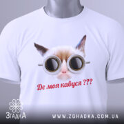 Футболка де моя кавуся. Біла футболка з принтом кота в окулярах, зображена зверху на столі. Принт чіткий, текст червоним кольором, на футболці є етикетка з зеленим шнурком.
