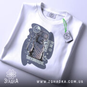 Футболка де ви навчалися, біла, зображена зверху, фон світло-сірий, принт з зображенням людини, що піднімає руку, з текстом і графічними елементами, на комірці є етикетка.