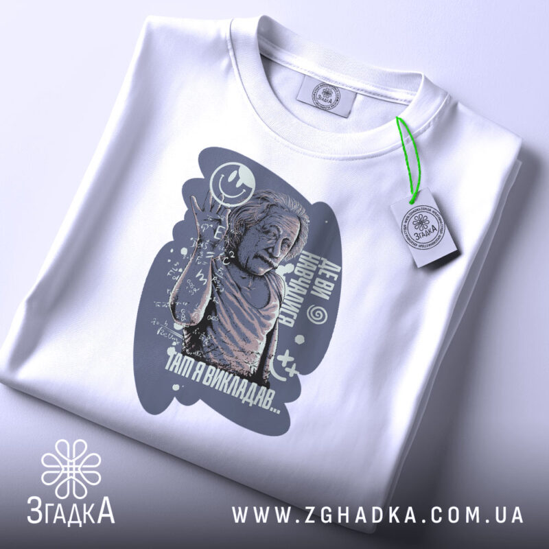 Футболка де ви навчалися, біла, зображена зверху, фон світло-сірий, принт з зображенням людини, що піднімає руку, з текстом і графічними елементами, на комірці є етикетка.