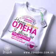 Футболка день народження, біла, лежить на столі, фон світлий, принт з текстом на українській мові, кольори: рожевий, жовтий, чорний, фіолетовий, на футболці є етикетка.