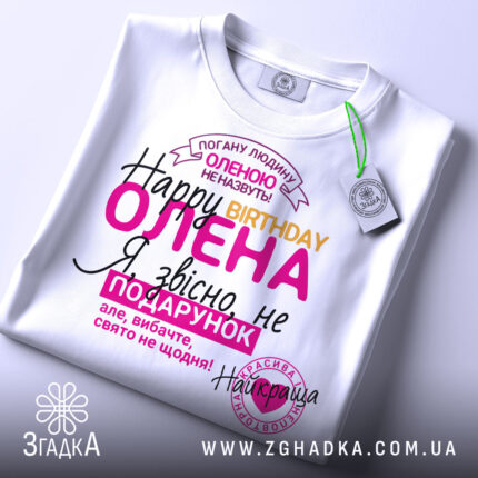 Футболка день народження, біла, лежить на столі, фон світлий, принт з текстом на українській мові, кольори: рожевий, жовтий, чорний, фіолетовий, на футболці є етикетка.