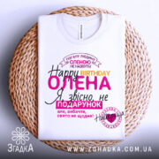 Футболка день народження, біла, лежить на плетеній кошику, фон нейтральний, принт містить текст на українській мові, кольори: рожевий, жовтий, чорний, фіолетовий.