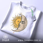 Футболка день ніч, біла, зображена з верхнього ракурсу, фон світло-сірий, принт з сонцем і місяцем, що зображують обличчя, жовті та сірі деталі, з етикеткою на зеленому шнурку.