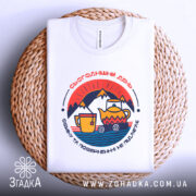 Футболка день обміну не підлягає. Біла футболка з округлим вирізом, зображена зверху на плетеній основі. На фоні світло-сірий колір. Принт містить кольорові елементи, зокрема чайник і чашку, оформлені в стилі графіки.