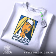 Футболка дякую за п`ятницю, біла, складена на поверхні, фон світло-сірий, принт зображає жінку в хустці, яка тримає палець на губах, кольори принта жовтий, синій та оранжевий, з етикеткою на шнурку.