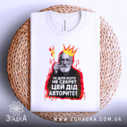 Футболка дід авторитет, біла, зображена зверху на плетеній основі, фон світлий, принт з зображенням чоловіка з бородою, короною та червоними вогнями, текст на українській мові.