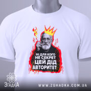 Футболка дід авторитет, біла, зображена з верхнього ракурсу, на фоні світло-сірого градієнта, принт з зображенням чоловіка з бородою, короною та червоними вогнями, текст на українській мові, з зеленим ярликом.