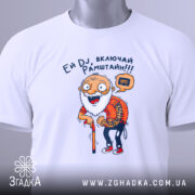 Футболка дід хоче Рамштайн, біла, складена на столі, фон світло-сірий, принт з дідусем у червоній сорочці в клітинку, який тримає палицю, з етикеткою на комірці, текст 'Ей DJ, включай Рамштайн!!!'.