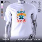 Футболка дідусь мій герой, біла, зображена на манекені, фон світло-сірий, принт кольоровий з написом 'ДІДУСЬ МІЙ ГЕРОЙ!' та зображенням щита і блискавки.