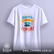 Футболка дідусь мій герой, біла, підвішена на вішалці, фон світло-сірий, принт кольоровий з написом 'ДІДУСЬ МІЙ ГЕРОЙ!' та зображенням щита і блискавки.