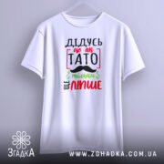 Футболка дідусь це як тато, біла, зображена з фронтального ракурсу, фон світло-сірий, принт з червоним, зеленим і чорним текстом, що говорить 'ДІДУСЬ ЦЕ ЯК ТАТО ТІЛЬКИ ЩЕ ЛІПШЕ' з малюнком вусів.