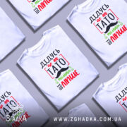 Футболка дідусь це як тато, біла, зображена з правого ракурсу на манекені, фон світло-сірий, принт з червоним, зеленим і чорним текстом, що говорить 'ДІДУСЬ ЦЕ ЯК ТАТО ТІЛЬКИ ЩЕ ЛІПШЕ' з малюнком вусів.