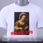 Футболка діджей дівчина, біла, зображена зверху, фон світлий, принт з портретом дівчини в навушниках, текст червоним шрифтом 'ЗАРАЗ БУДЕ ГАРЯЧЕ', на комірці видно етикетку.