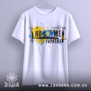 Футболка дім Україна, біла, підвішена на вішалці, фон світло-сірий, принт з жовто-блакитними кольорами, зображення соняшника та абстрактні елементи.