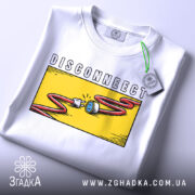 Футболка disconnect стиль, біла, складена на поверхні, фон світлий, принт з жовтим фоном, червоним кабелем і розеткою, з етикеткою на шнурку.