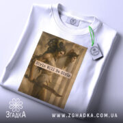 Футболка дівчата можуть бути білого кольору, складена на поверхні з видимим етикеткою. Принт з зображенням двох жінок та текстом "Girls Will Be Girls" займає центральну частину футболки.