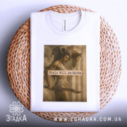 Футболка дівчата можуть бути білого кольору, складена на плетеній основі. Принт з зображенням жінок та текстом "Girls Will Be Girls" займає центральну частину, а етикетка видима вгорі.