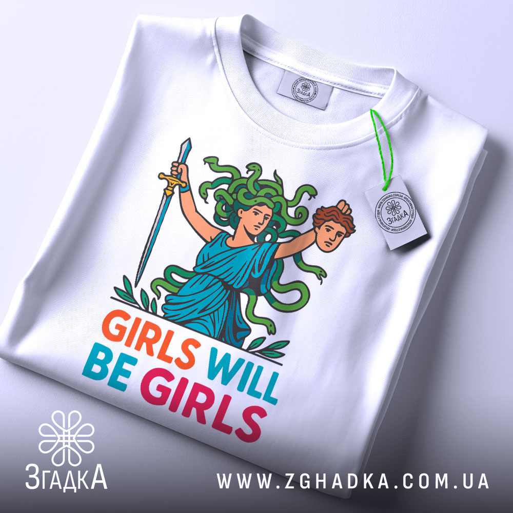 Футболка дівчата такі дівчата, біла, зображена з верхнього ракурсу, фон світло-сірий, принт з дівчиною з зеленим волоссям, що тримає меч і голову, текст 'GIRLS WILL BE GIRLS' яскравих кольорів, на футболці є етикетка.