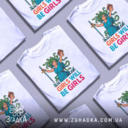 Футболка дівчата такі дівчата, біла, зображена з близького ракурсу, фон світло-сірий, принт з дівчиною з зеленим волоссям, що тримає меч і голову, текст 'GIRLS WILL BE GIRLS' яскравих кольорів.