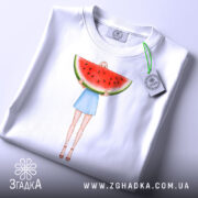 Футболка дівчина кавун, біла, з верхнього ракурсу, на фоні світло-сірого, принт з дівчиною у блакитній спідниці, яка тримає кавун, з етикеткою на шнурку.