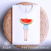 Футболка дівчина кавун, біла, з верхнього ракурсу, на фоні плетеного кошика, принт з дівчиною у блакитній спідниці, яка тримає кавун, складена на столі.