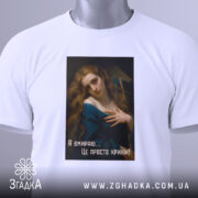 Футболка дівчина кринж, біла футболка, складена на поверхні, принт з дівчиною у блакитному платті, текст 'Я вмираю... Це просто кринж!' на чорному фоні, зелена етикетка на комірці, фон світлий.