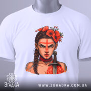 Футболка Дівчина Войовниця, біла, складена на столі, фон світло-сірий, принт з зображенням дівчини з червоними квітами на голові та мечем, етикетка з зеленим шнурком.