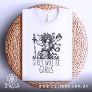 Футболка дівоча помста, біла, складена на плетеній кошику, фон світло-сірий, принт з дівчиною з мечем та написом 'GIRLS WILL BE GIRLS'.
