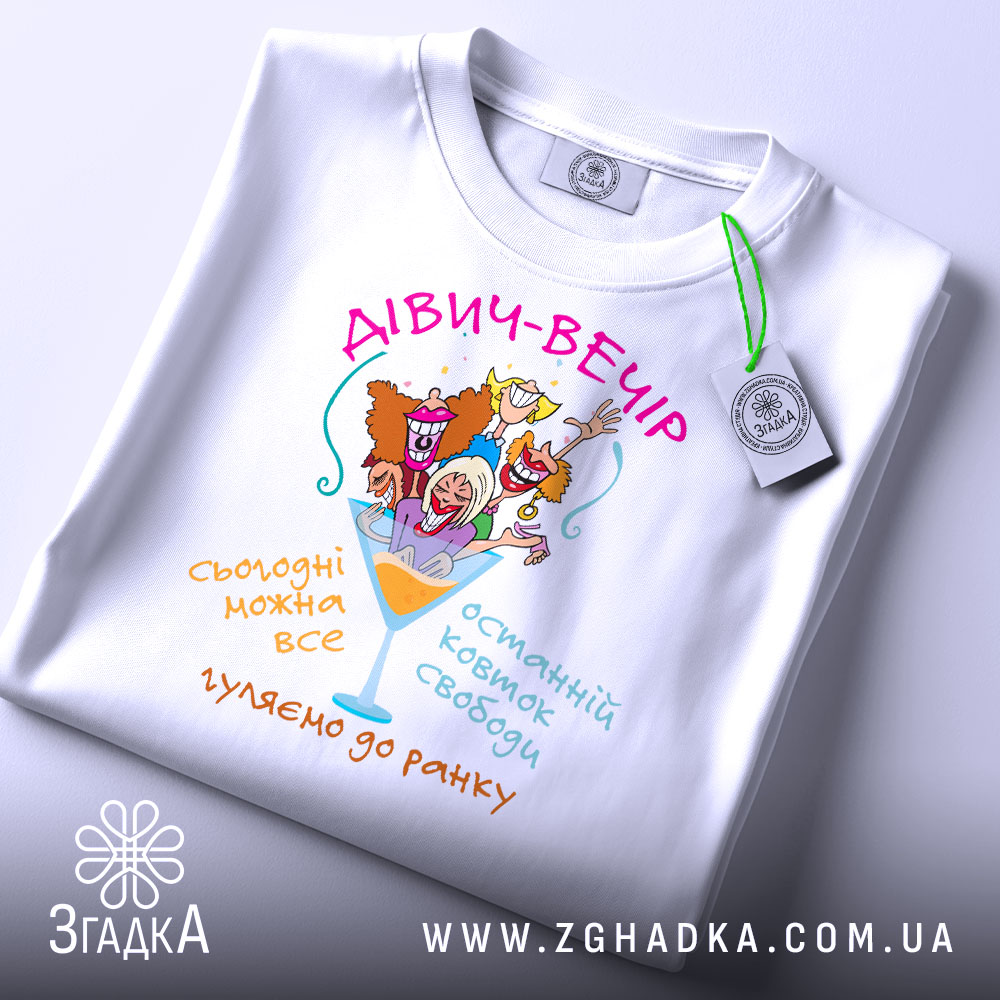 Футболка дівич-вечір білого кольору, зображена на столі, з принтом, що містить кольорові малюнки жінок у святкових капелюшках, текстом на українській мові, з етикеткою на комірці, фон світло-сірий.