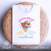 Футболка дівич-вечір білого кольору, зображена на плетеній кошику, з принтом, що містить кольорові малюнки жінок у святкових капелюшках, текстом на українській мові, фон світлий.