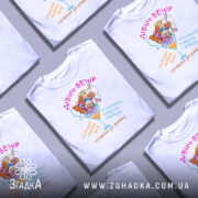 Футболка дівич-вечір білого кольору, зображена на манекені, з принтом, що містить кольорові малюнки жінок у святкових капелюшках, текстом на українській мові, фон світло-сірий.