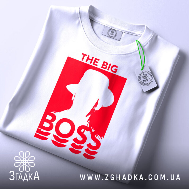 Футболка для босса, білого кольору, складена на столі, фон світло-сірий, принт червоного кольору з написом 'THE BIG BOSS' та силуетом людини в капелюсі, на футболці прикріплена етикетка.