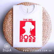 Футболка для босса, білого кольору, складена на плетеній кошику, фон білий, принт червоного кольору з написом 'THE BIG BOSS' та силуетом людини в капелюсі.