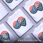 Футболка для мандрівників. Біла футболка з коротким рукавом, зображена з фронтального ракурсу. На грудях великий принт у формі серця з горами, лісом та логотипом 'GO'. Фон нейтральний, що підкреслює яскравість принта.