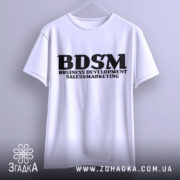 Футболка для маркетолога, білого кольору, підвішена на вішалці, фон світло-сірий, принт чорного кольору з написом 'BDSM BUSINESS DEVELOPMENT SALES & MARKETING'.