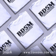 Футболка для маркетолога, білого кольору, зображена на манекені з блискучою поверхнею, фон світло-сірий, принт чорного кольору з написом 'BDSM BUSINESS DEVELOPMENT SALES & MARKETING'.