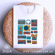 Футболка для меломана, білого кольору, складена на плетеній кошику, фон світло-сірий, принт з музичними елементами в яскравих кольорах, видно деталі принта та ярлик на горловині.