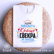 Футболка для найкращого свекра, білого кольору, зображена з верхнього ракурсу, лежить на плетеній основі, фон світлий, принт яскравий, з текстом "хочу півсвіту обійти Краще свекра не знайти".