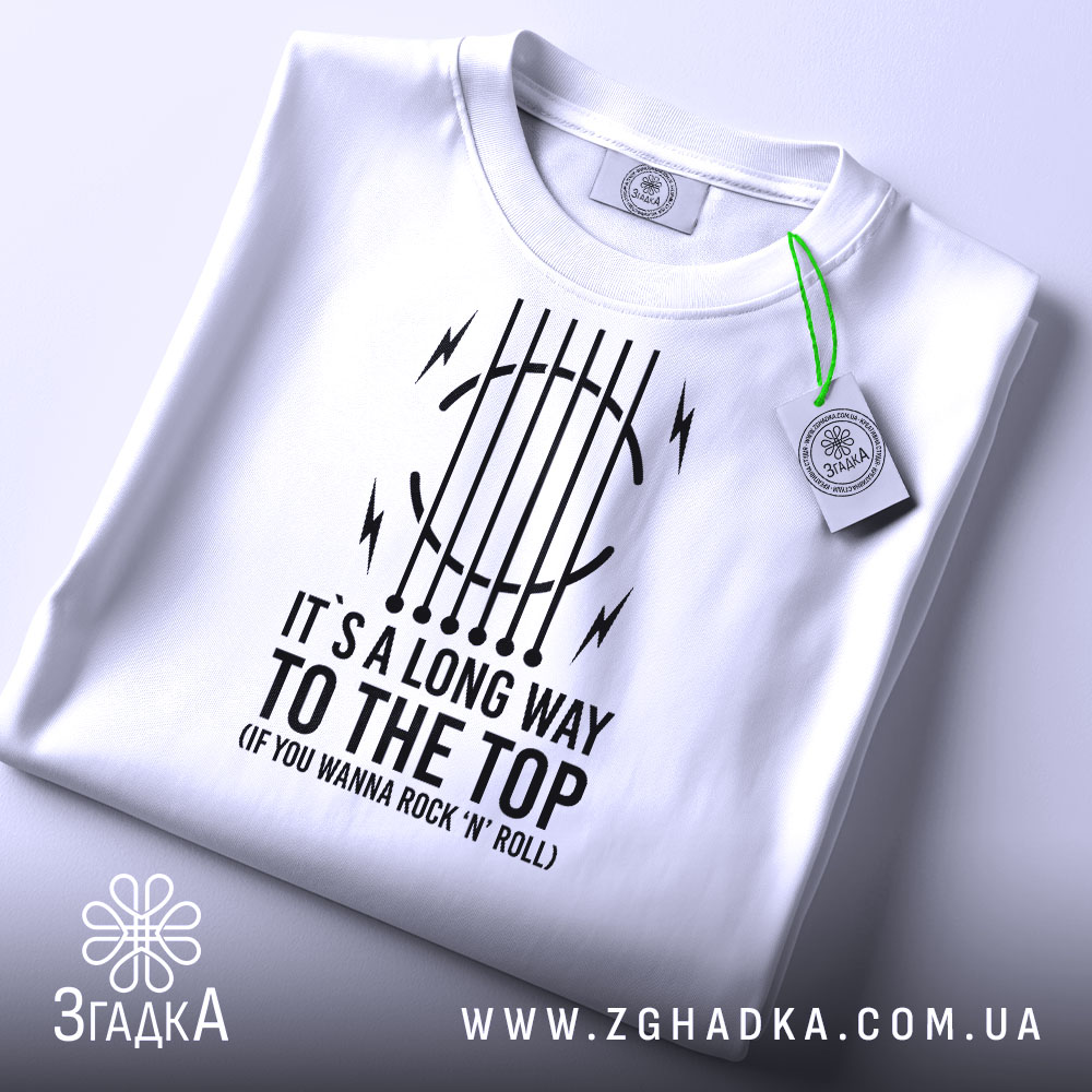 Футболка для рокера, біла, складена на поверхні, фон світлий, принт чорного кольору з текстом "IT'S A LONG WAY TO THE TOP (IF YOU WANNA ROCK 'N' ROLL)" та графічними елементами, на футболці підвісна етикетка.
